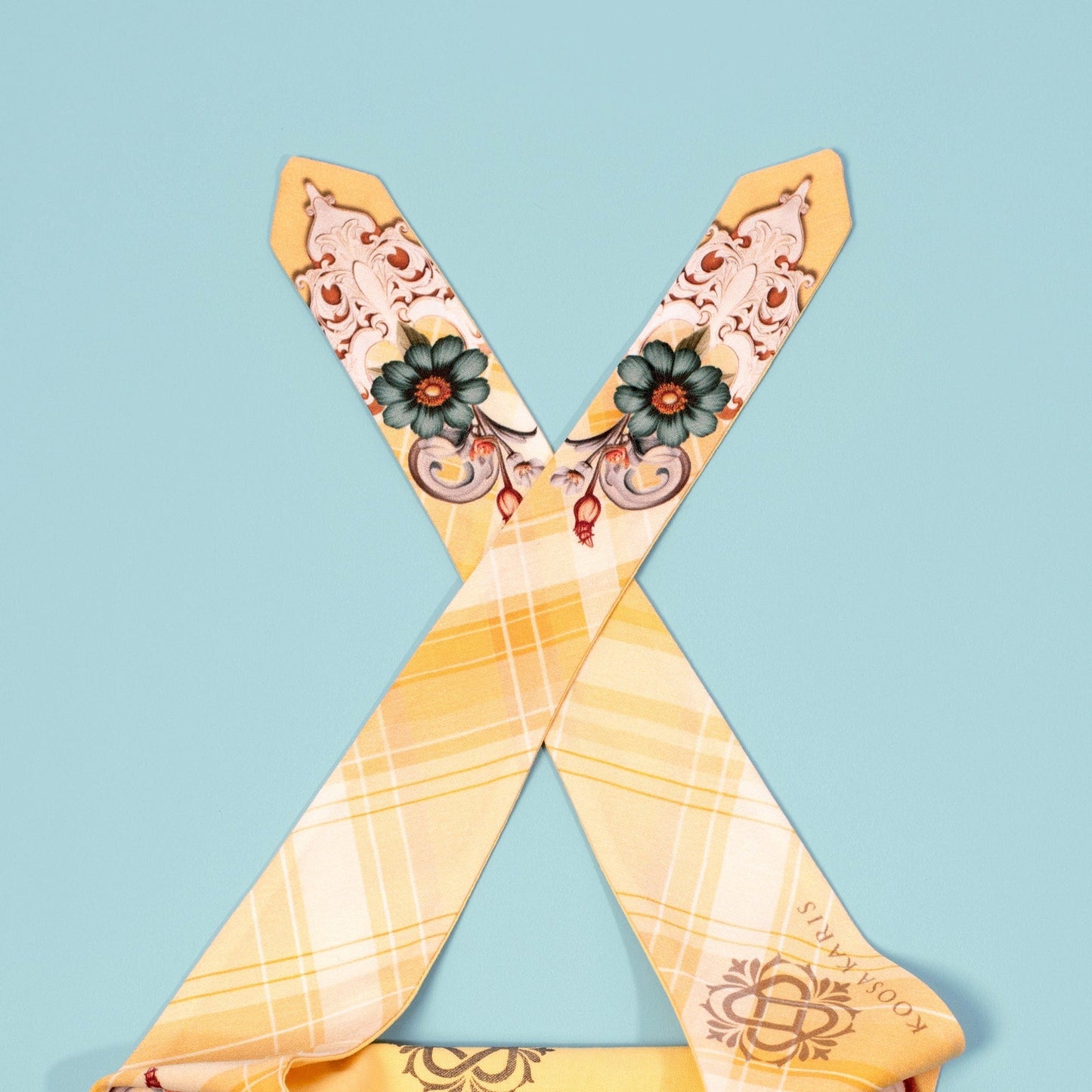 The tie ends of a yellow plaid dog bandana with a teal and white floral scroll pattern 